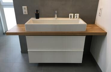 Moderner Badwaschtisch mit Holz-Arbeitsplatte, weißem rechteckigem Waschbecken und grauer Wand.
