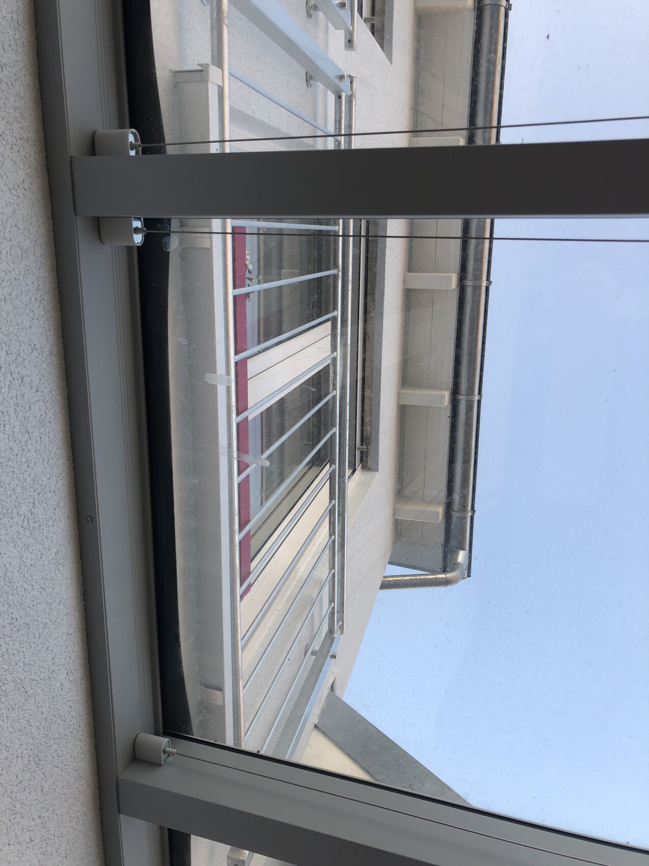 Fensterblick auf ein Metallbalkongeländer an der Gebäudefassade, Blick nach draußen zum Himmel