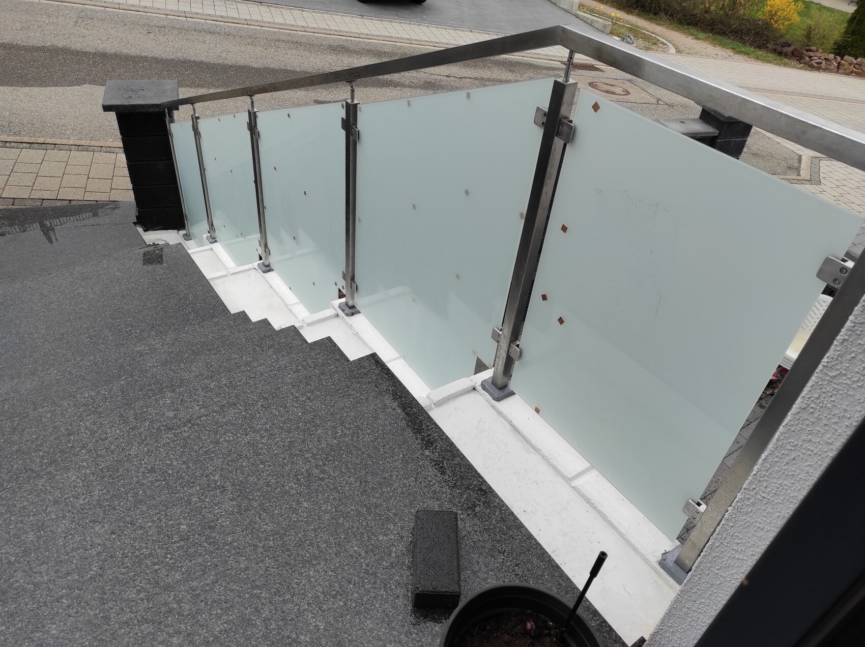Außenbereich einer Treppe mit Glasgeländer aus Glasplatten und Metallpfosten, Blick zur Straße.