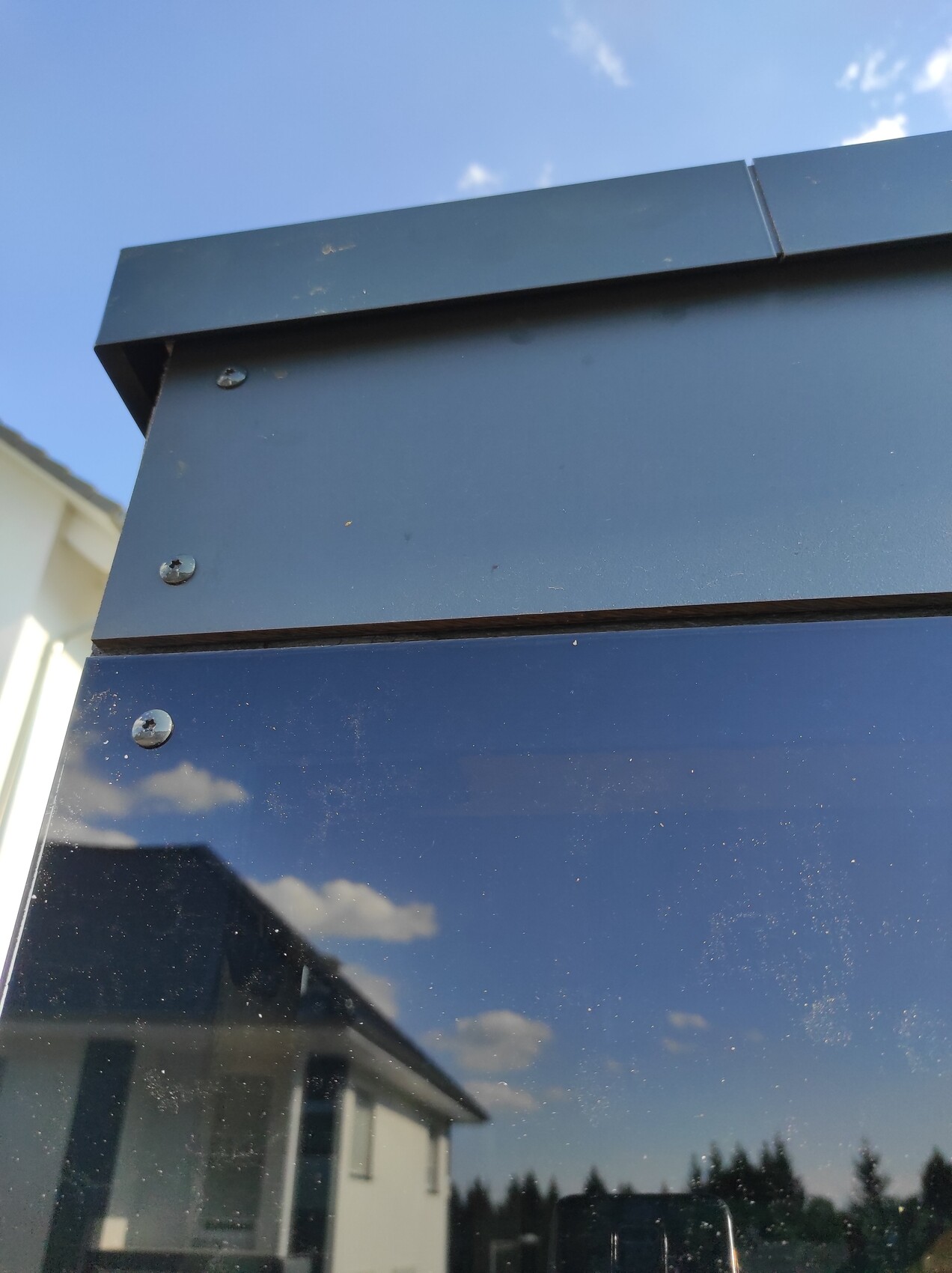Nahaufnahme einer blauen Metalloberfläche mit Schrauben; Spiegelung von Haus und blauem Himmel.