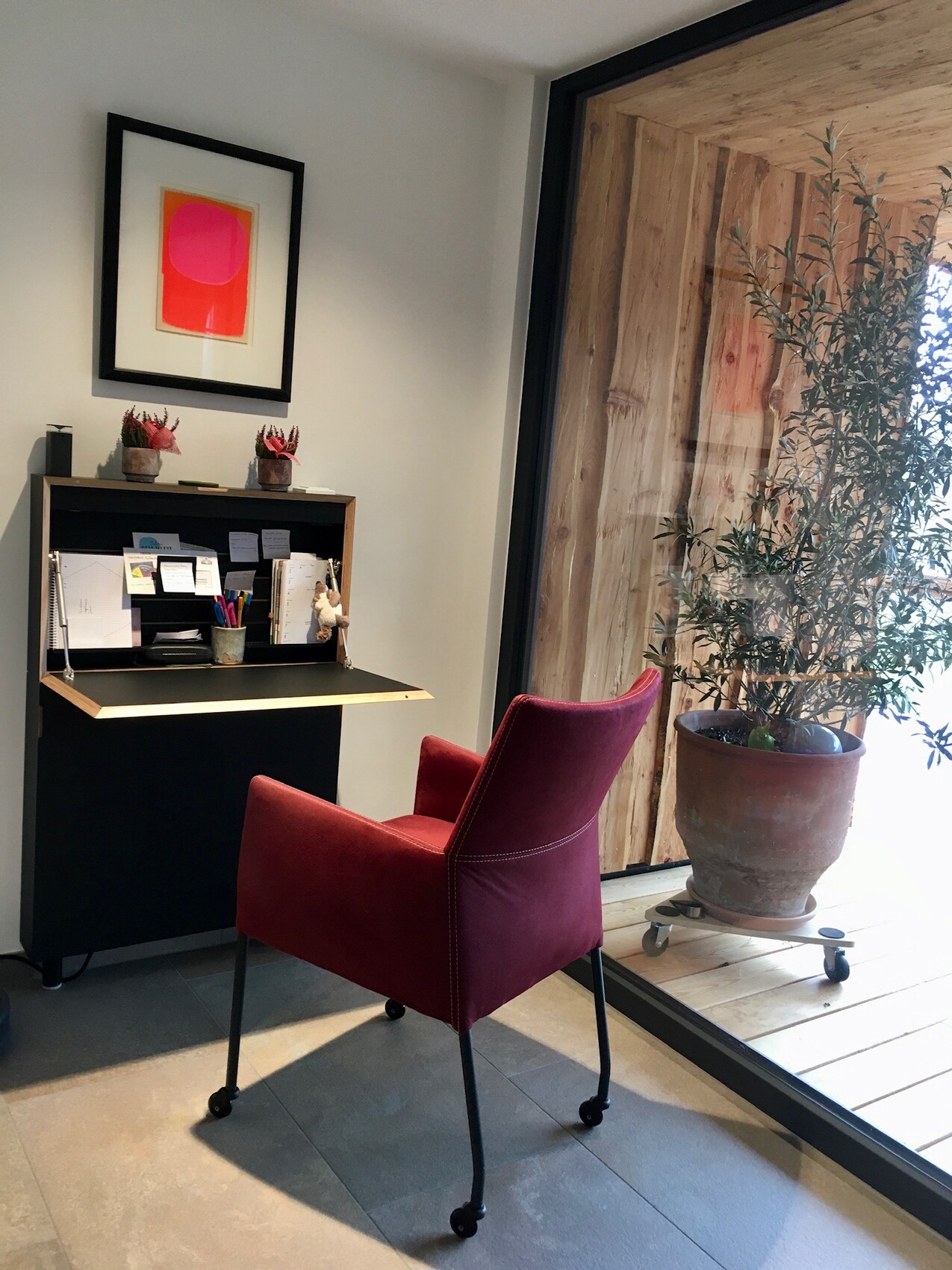 Büro-Ecke mit burgunderrotem Stuhl vor schwarzem Schreibtisch, Pflanze am Fenster.