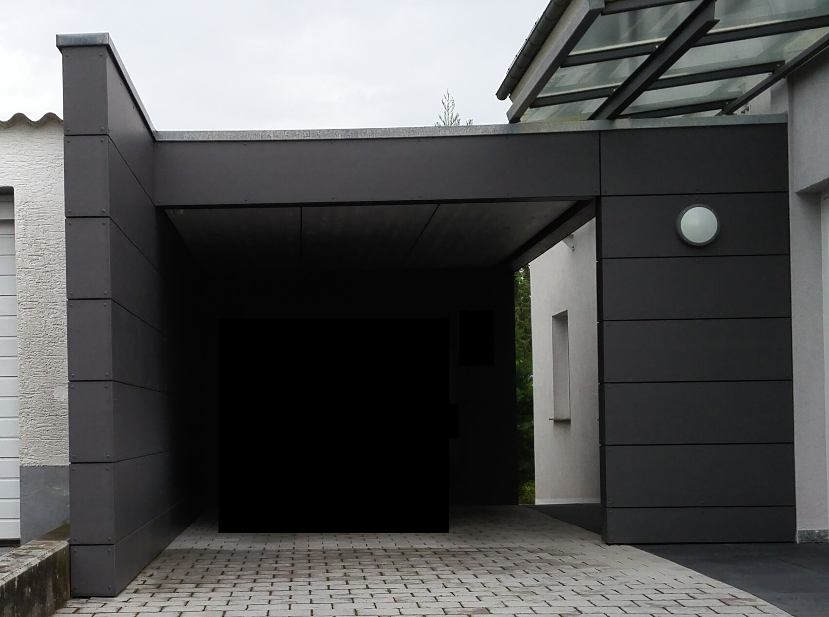 Moderner Carport mit dunkler Fassadenverkleidung und überdachter Zufahrt.