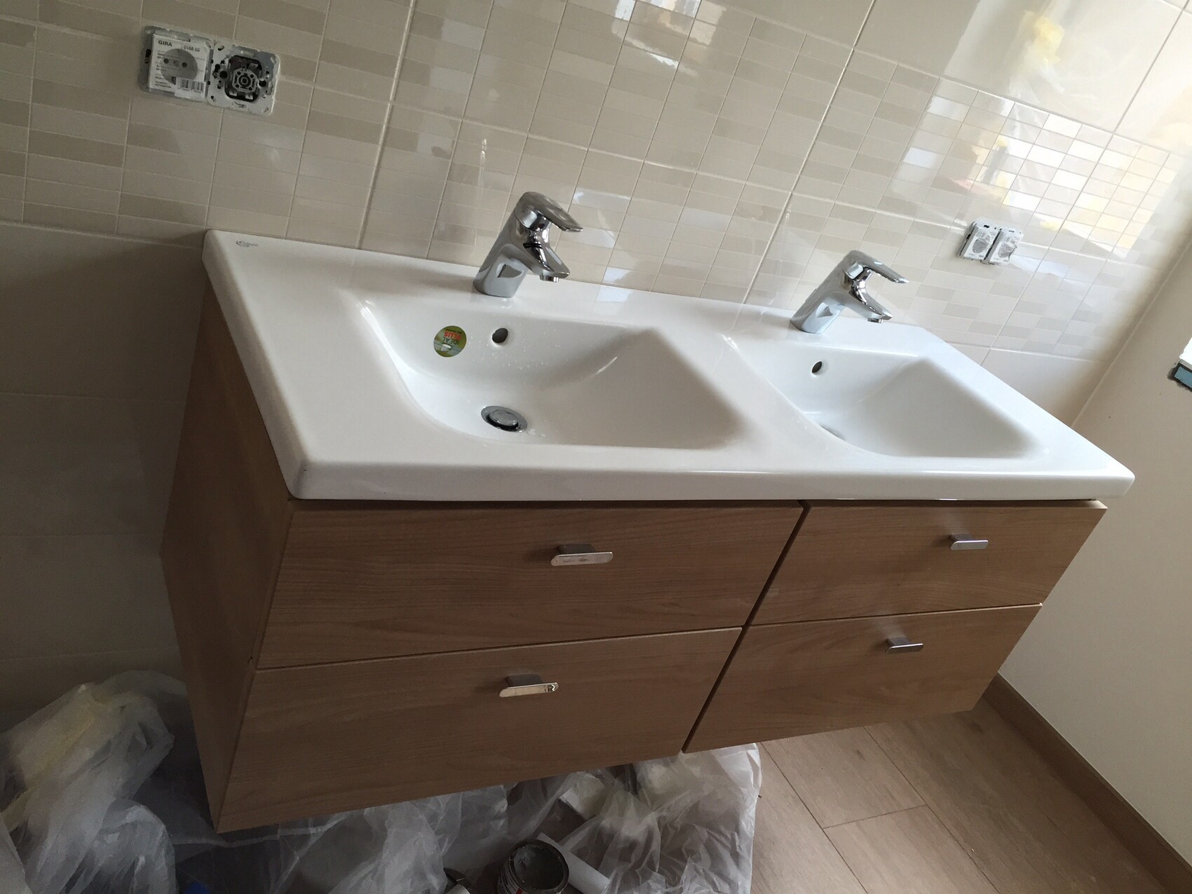 Doppelwaschbecken mit zwei Armaturen, Holzunterschrank und beige Fliesenwand im Badezimmer
