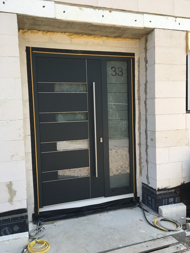 Moderne dunkle Haustür mit horizontalen Glasleisten; rechts die Nummer 33, Bauumgebung sichtbar.