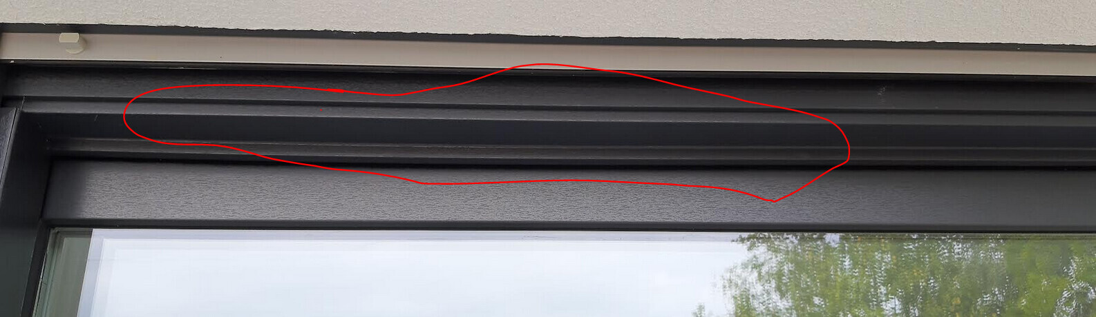 Nahaufnahme eines dunklen Rollladenrahmens über einem Fenster im Gebäude.