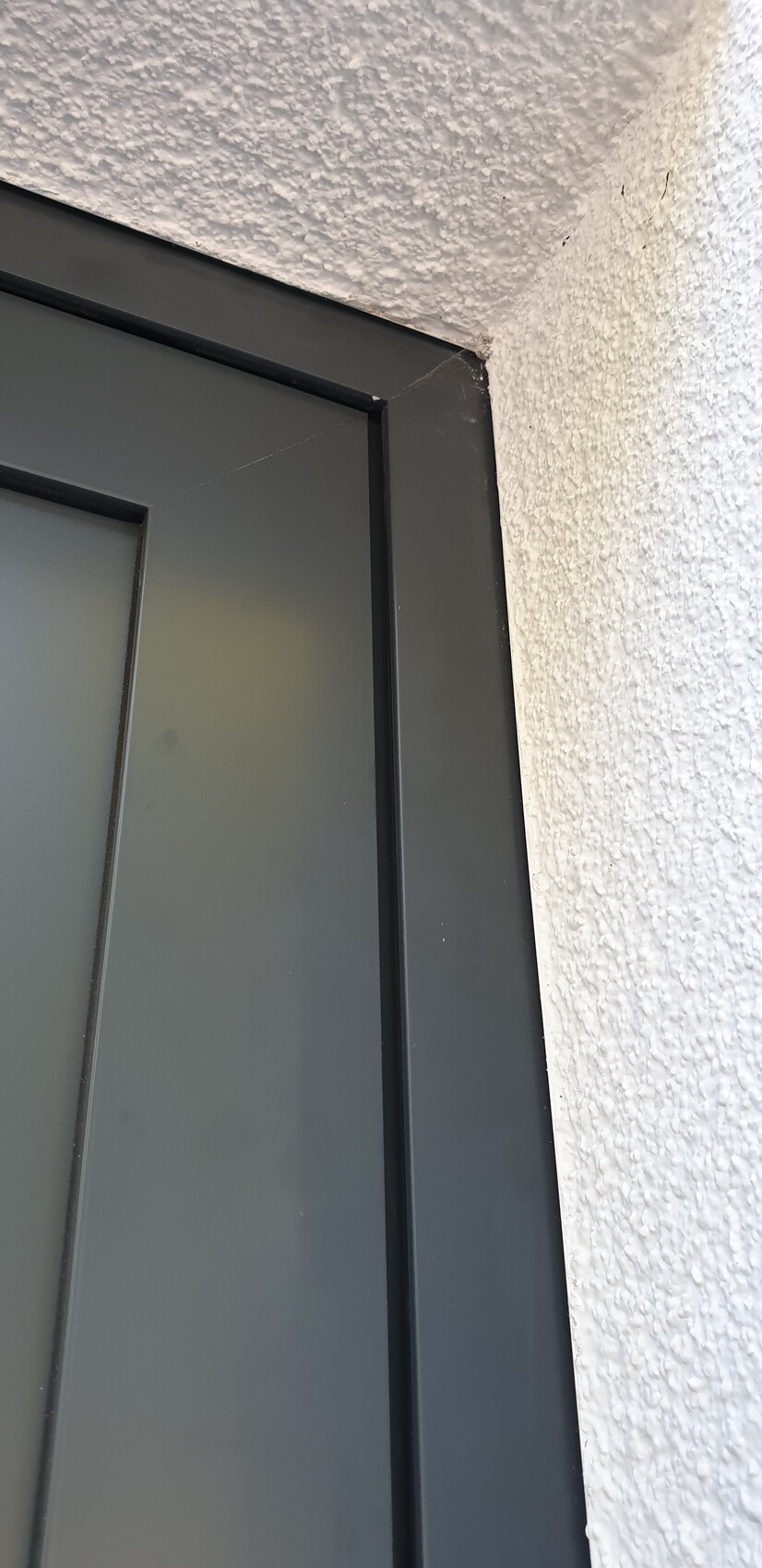 Nahaufnahme eines grauen Metallfensterrahmens an einer rauen weißen Wand, Ecke sichtbar.