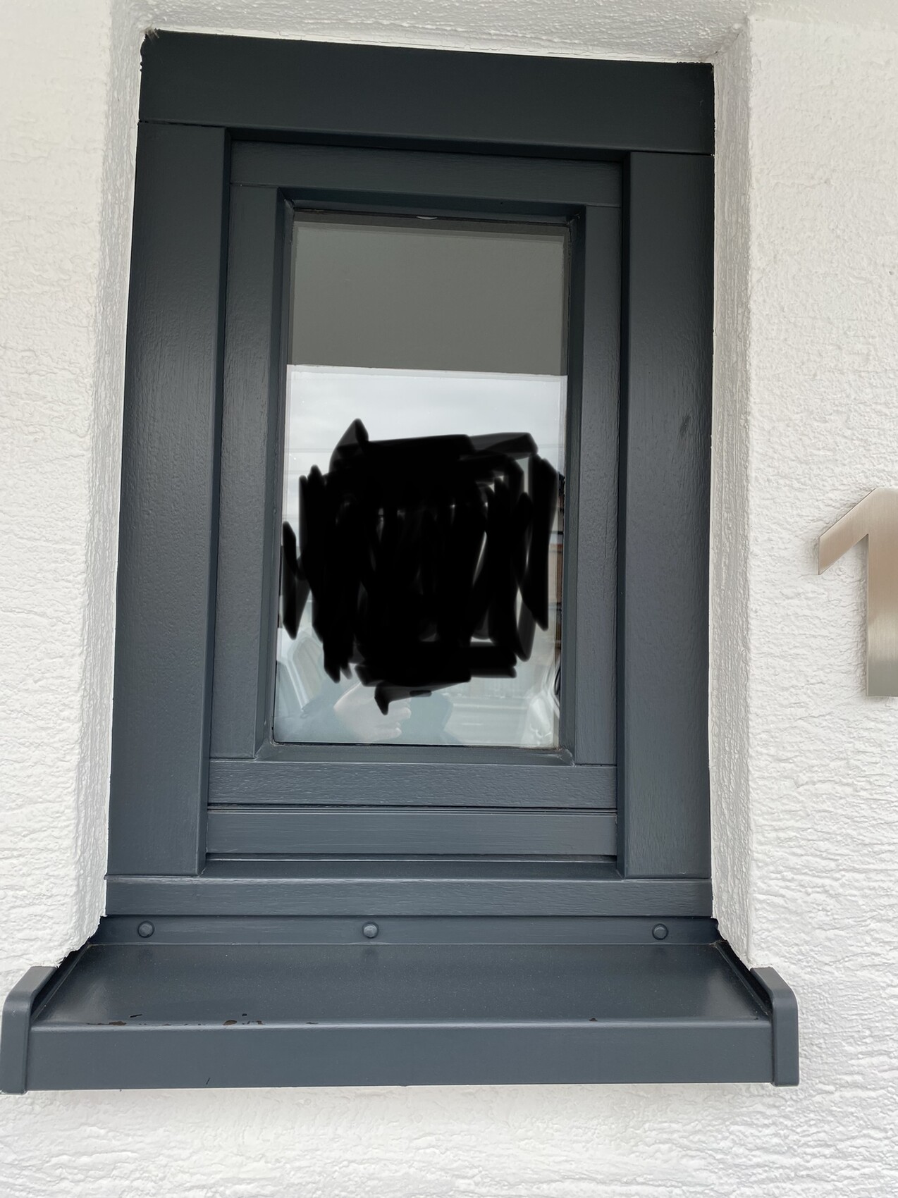 Vertikales Fenster in dunkelgrauem Rahmen vor Putzwand, Fensterbank, rechts Hausnummer 1.