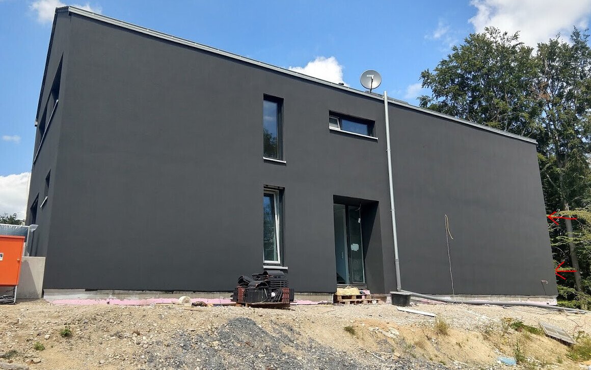 Modernes, dunkles zweigeschossiges Haus mit Flachdach im Bau; Baustellenmaterialien davor.