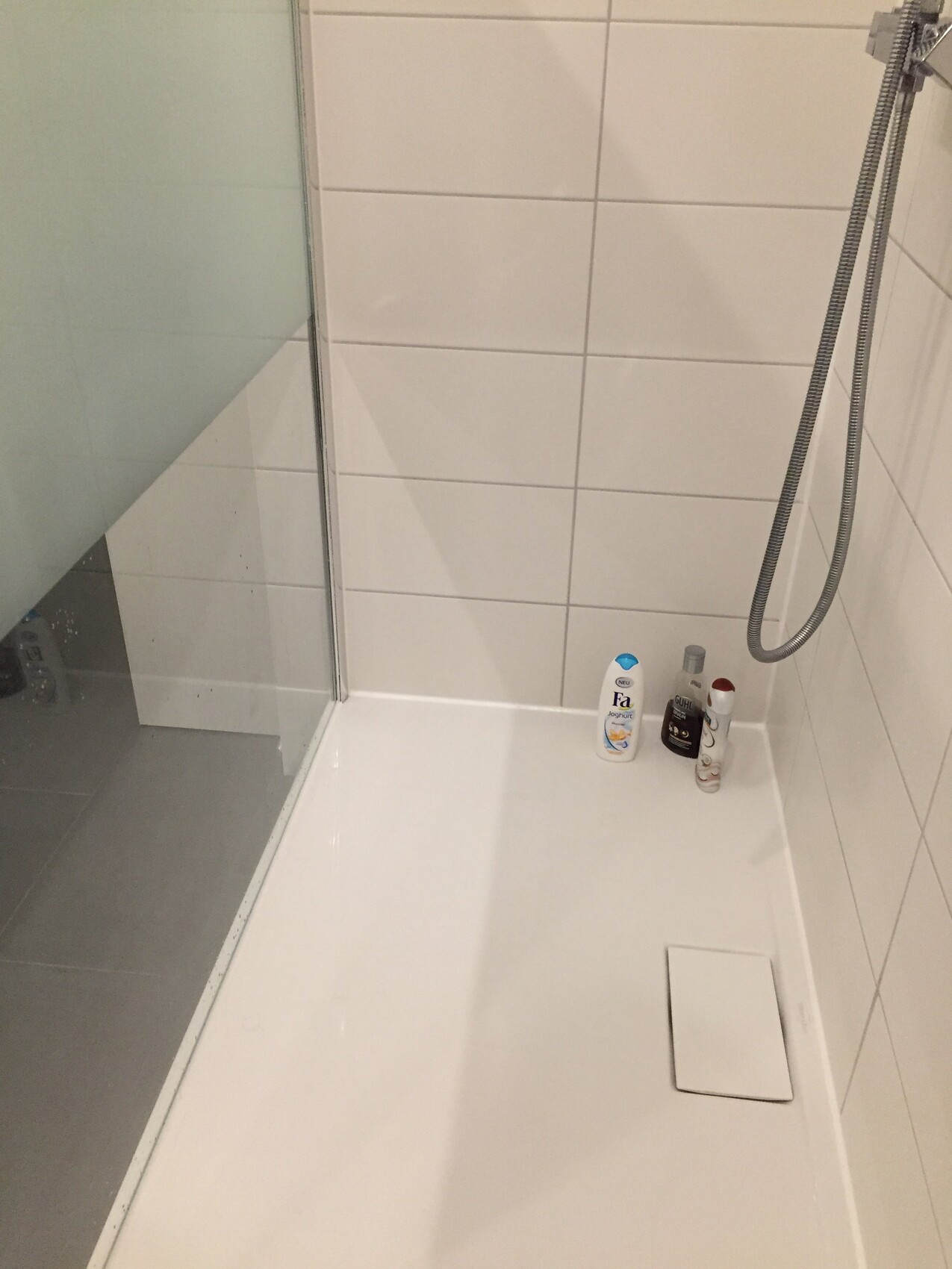 Dusche mit Glasabtrennung, weisse Fliesen und Badzubehoer am Boden
