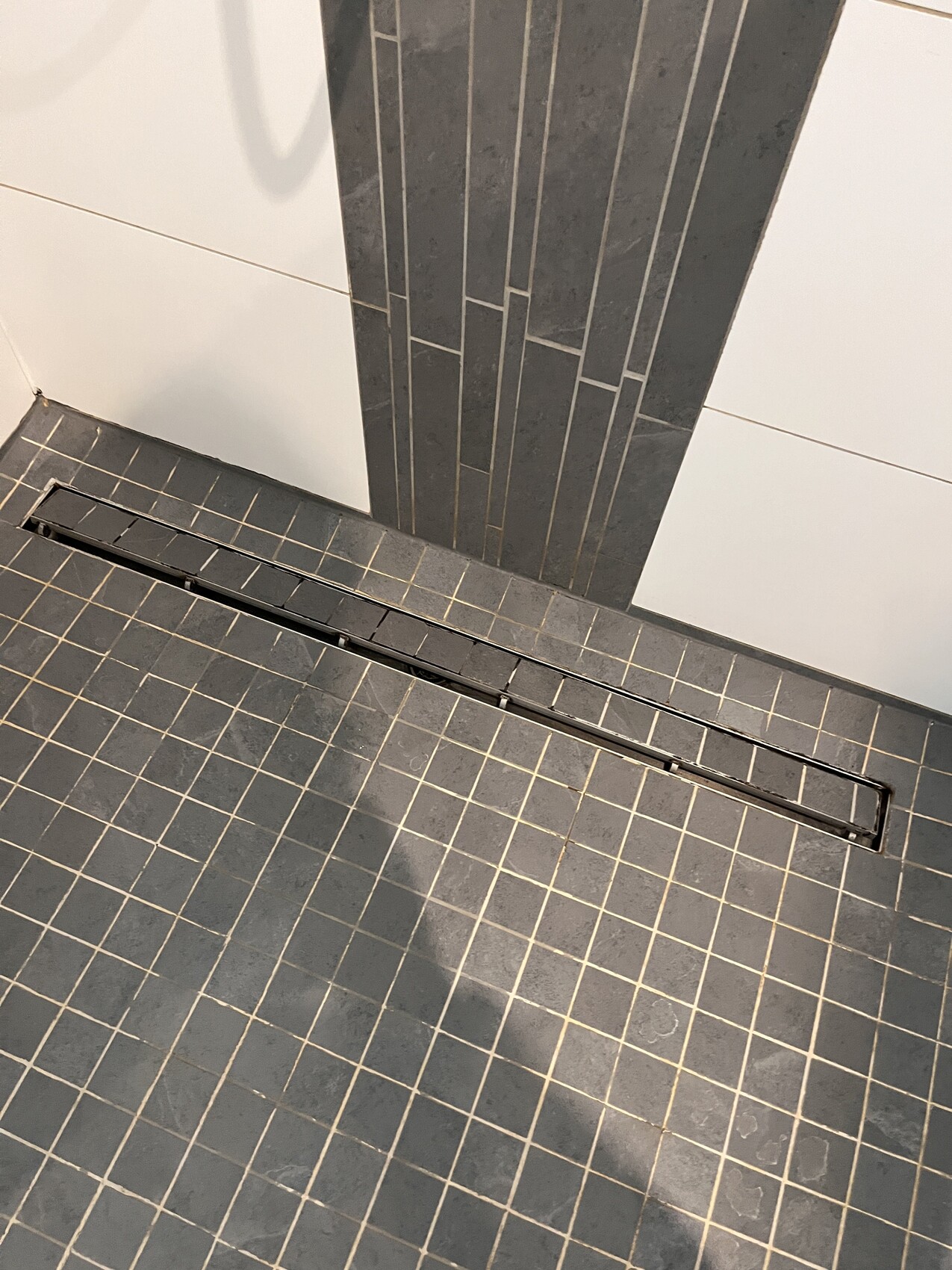 Dusche: rechteckige Abflussrinne im grauen Fliesenboden.