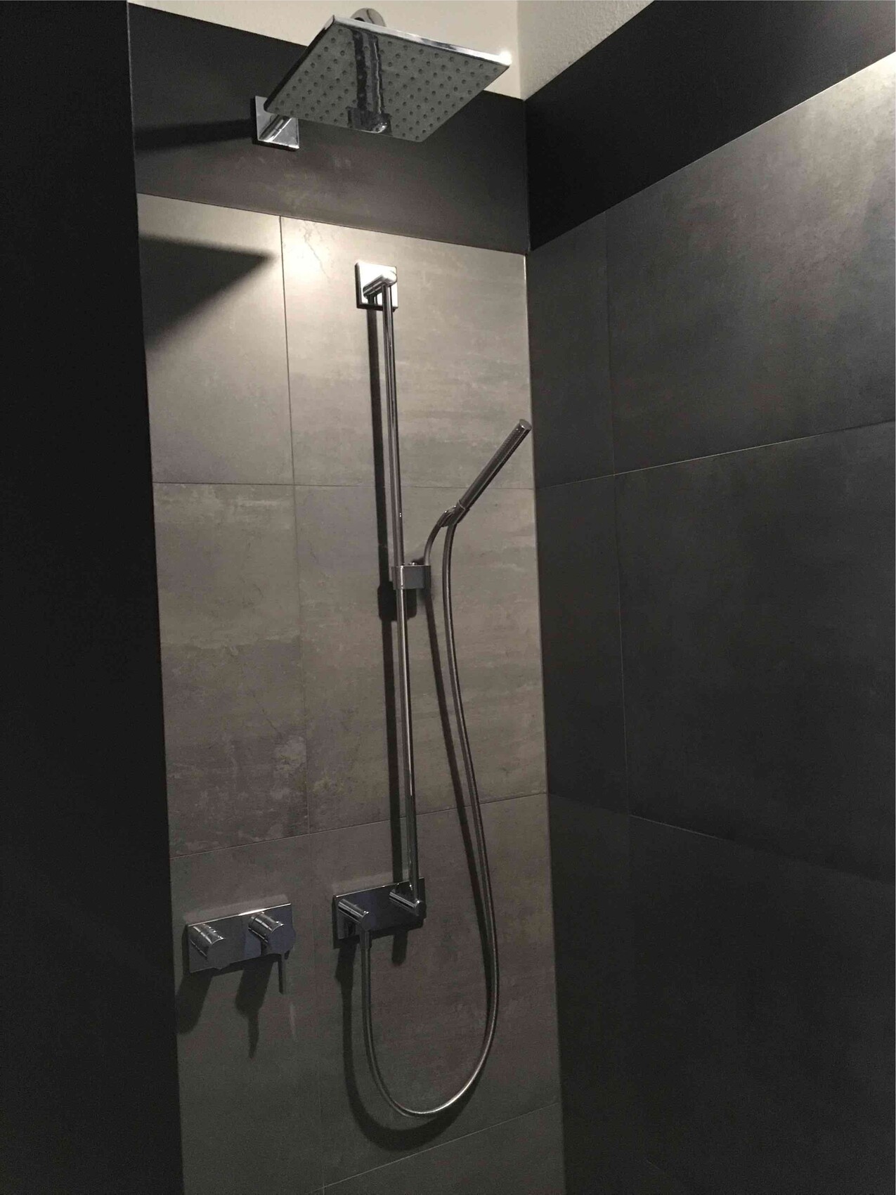 Moderne Dusche mit großer Regendusche, Handbrause und dunklen Fliesen.