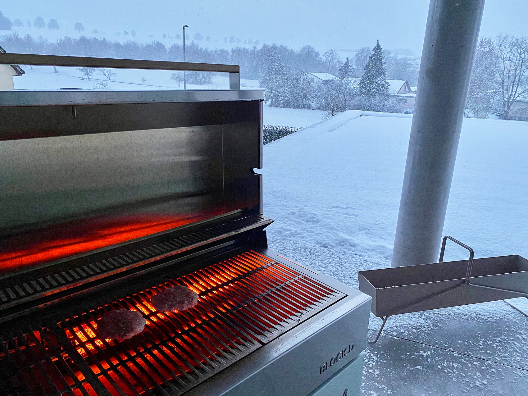 Gasgrill im Freien brutzelt zwei Burger-Patties; Schnee bedeckt die Umgebung.