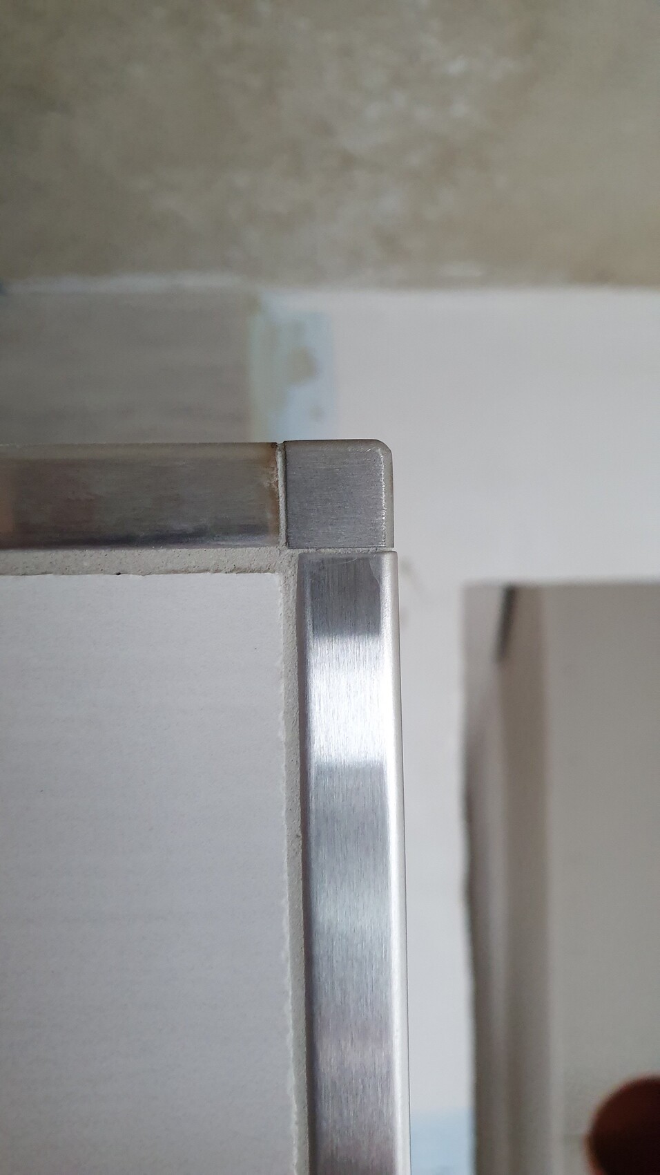 Nahaufnahme einer silbernen Metallkante an einer weißen Möbelfront, Ecke sichtbar