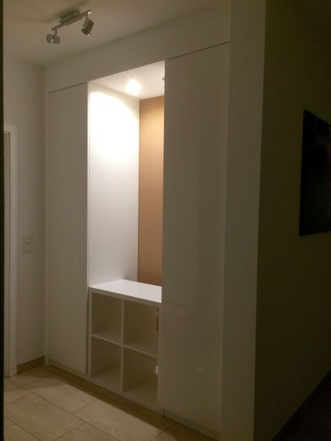 Moderne weiße Einbau-Garderobe im Flur mit offenen Würfelfächern unten und Beleuchtung.
