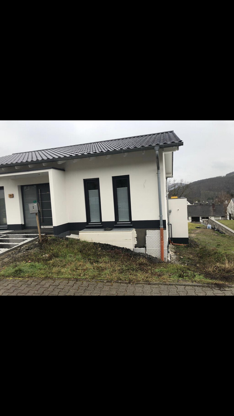 Modernes Einfamilienhaus mit weißer Fassade, schwarzem Sockel und dunklen Fensterrahmen.