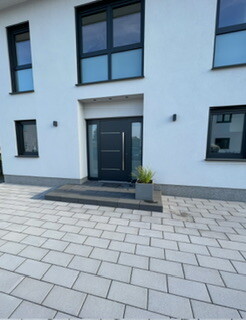 Moderne weiße Fassadenfront mit schwarzer Eingangstür, Pflasterweg und Pflanzkübel.