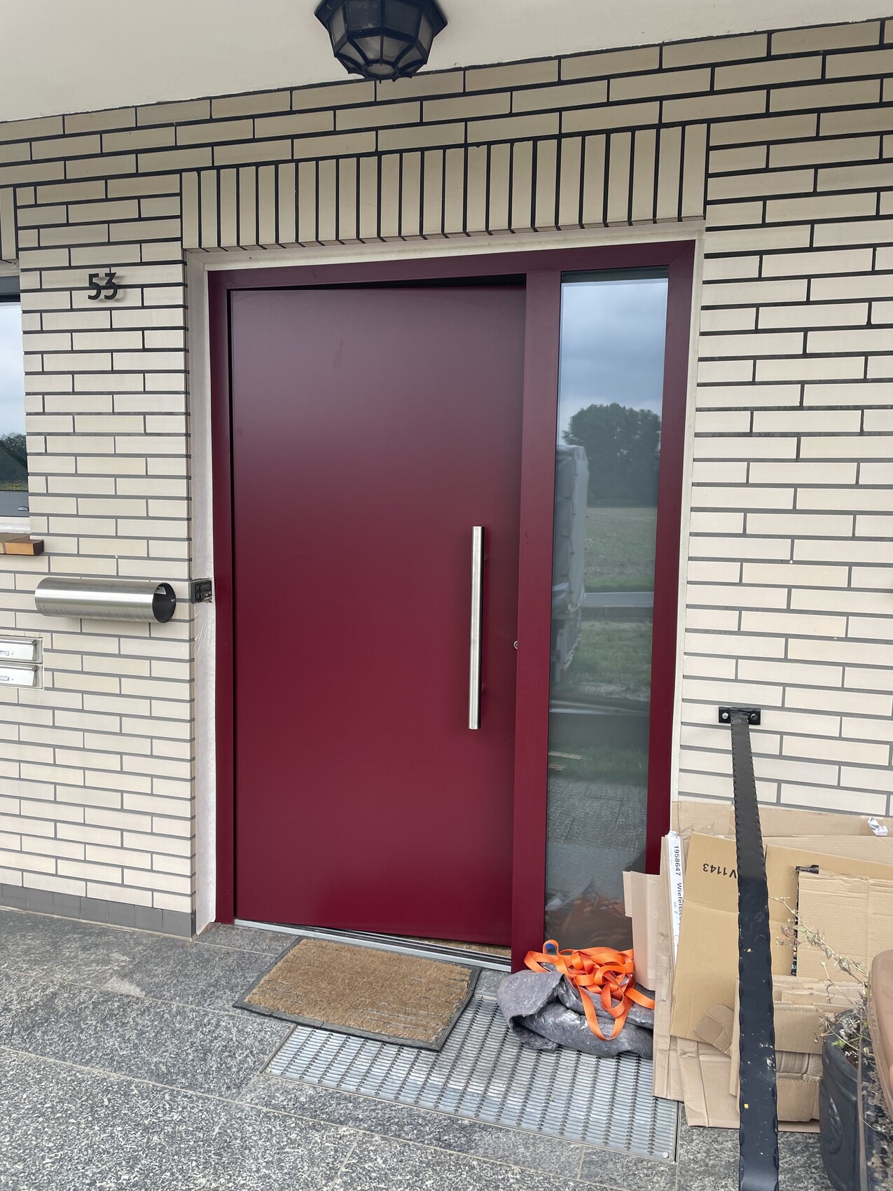 Türfront in burgunderrot mit seitlichem Glasfenster; Eingang mit Paketen daneben