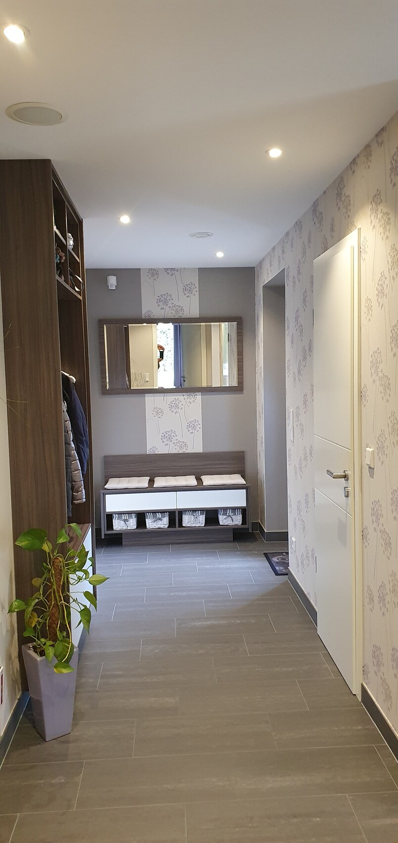 Flur mit Garderobe links, Bank und Aufbewahrungskästen, Spiegel, florale Tapete.
