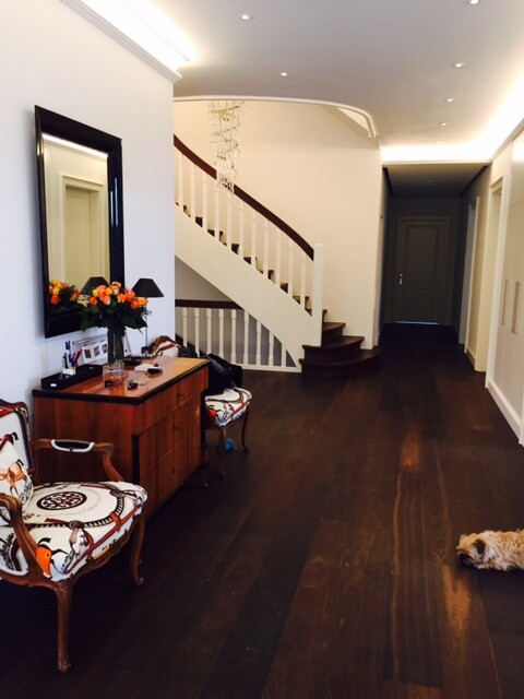 Heller Flur mit dunklem Holzboden, Treppe, Spiegel, Kommode mit Blumen, zwei Stühle, Hund am Boden
