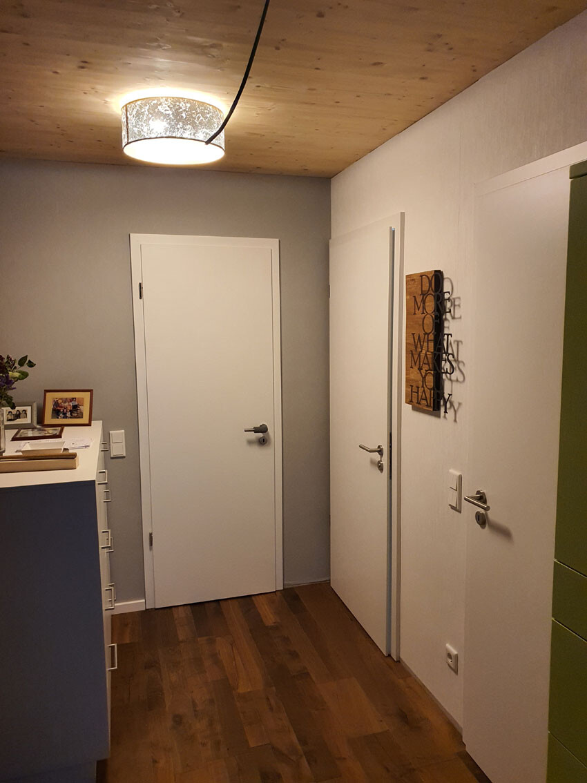 Flur mit Holzboden, runder Deckenlampe, weißen Türen, Wandkunst und Kommode mit Fotos.