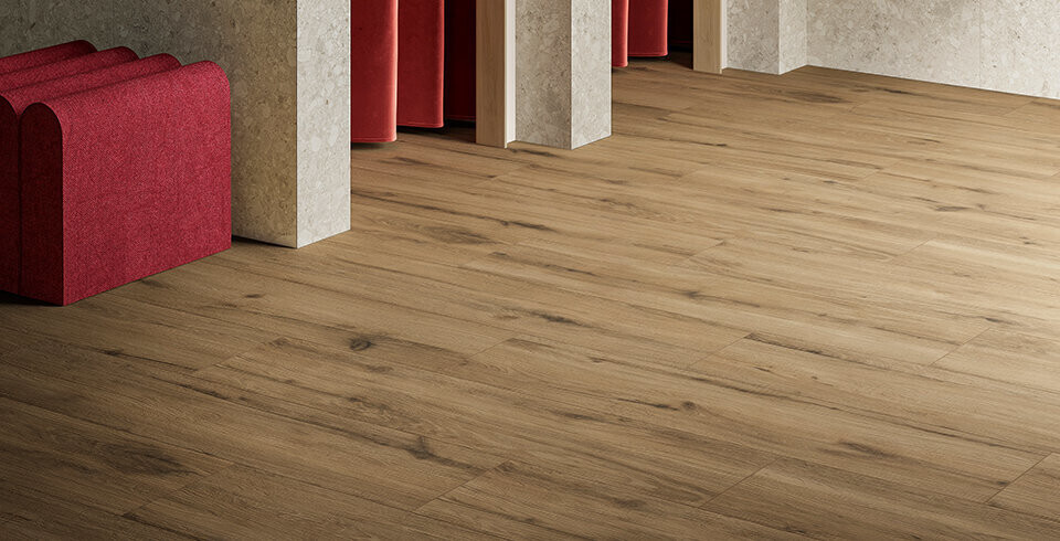 Holzboden mit roten Sesseln entlang heller Säulen im Saal.