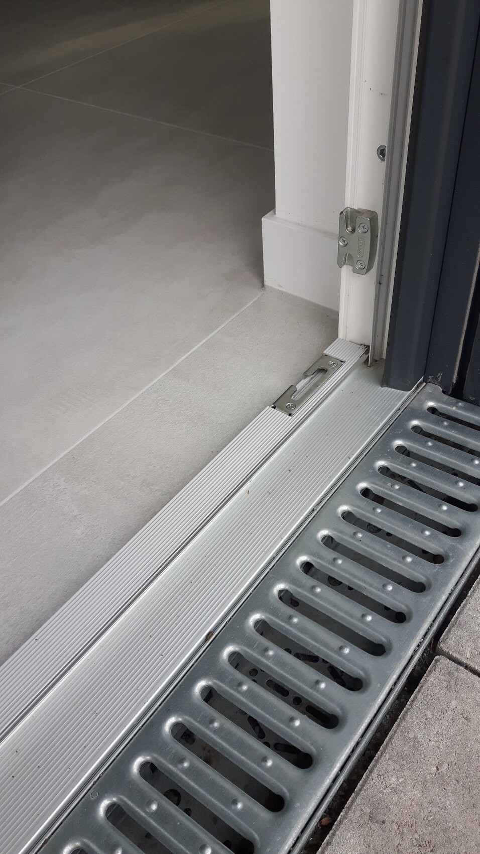 Türdurchgang: Innenbereich mit hellen Fliesen, außen Metallrinnen-Drainage am Eingang.