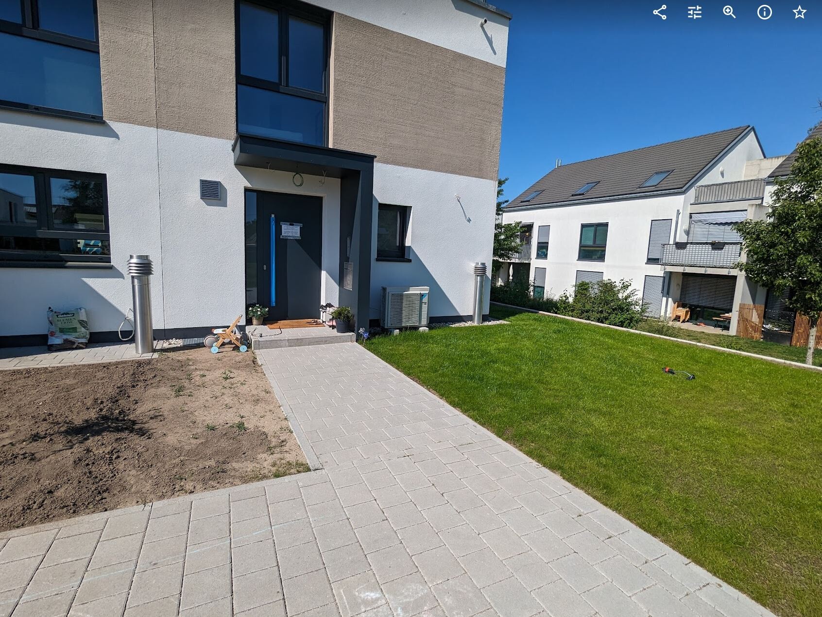 Modernes Mehrfamilienhaus: Eingang mit gepflastertem Weg und grünem Hofgarten vor der Tür