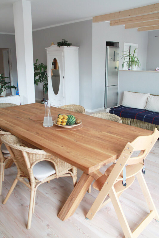 Heller Essbereich mit Holztisch, Stühlen, Obstschale, Karaffe, weißem Schrank und Sofa.