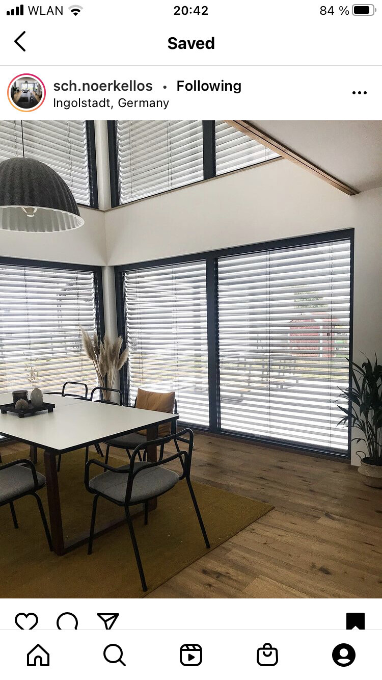 Moderner Essbereich: weißer Tisch, schwarze Stühle, große Fenster mit Jalousien, Pampasgras.