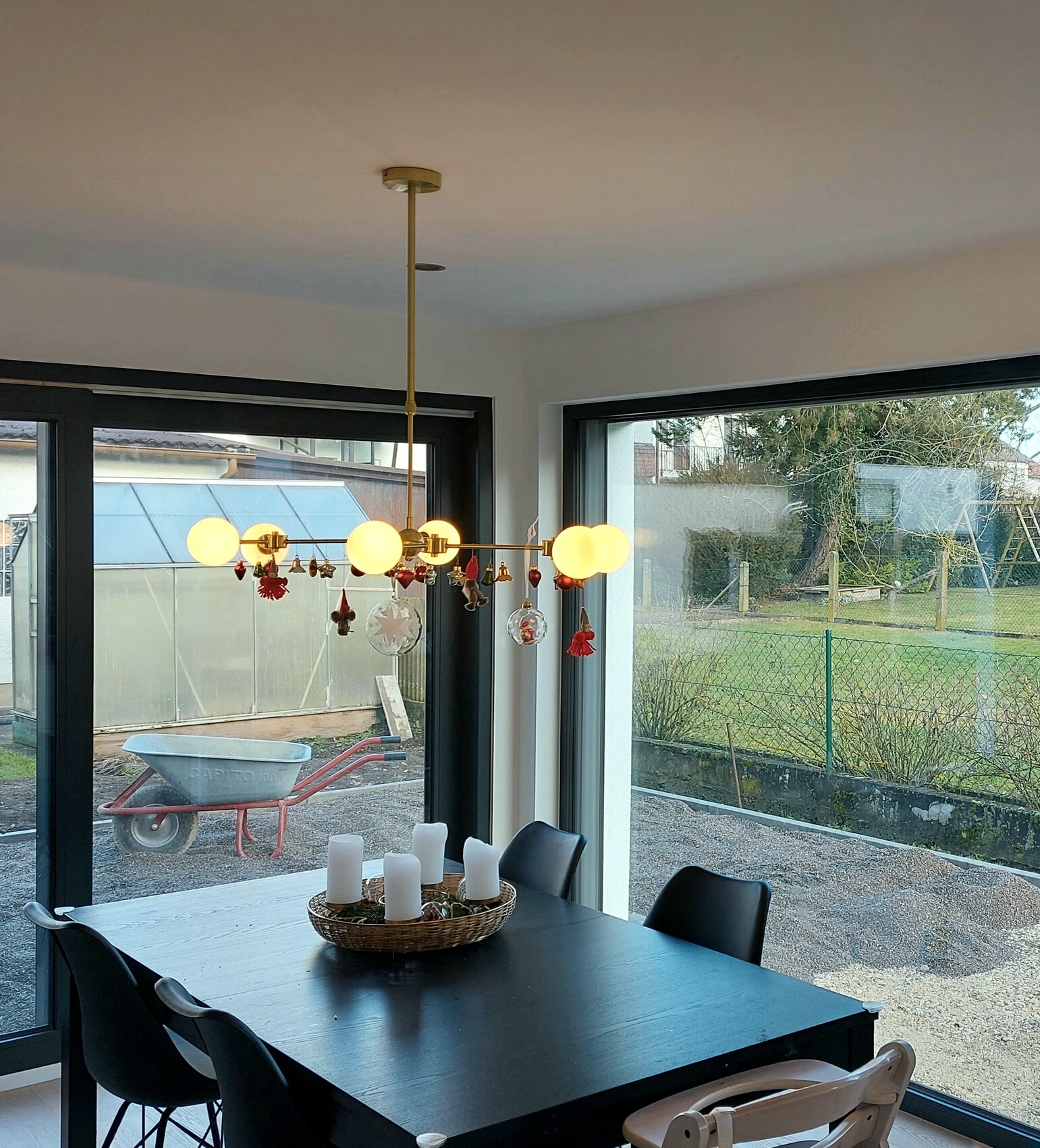 Heller Esstisch mit schwarzer Oberfläche und Kugellampe; Kerzen im Korb, Gartenaussicht durch Fenster.