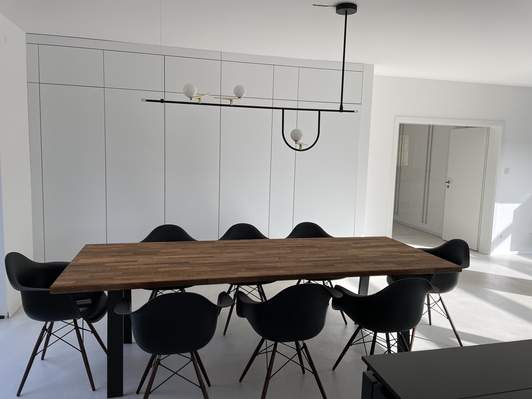 Modernes Esszimmer mit langem Holztisch, schwarzen Sesseln und weißen Schränken.