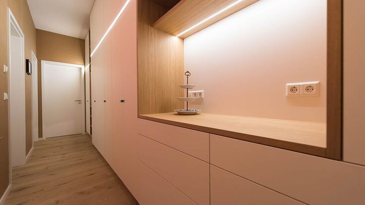 Heller Flur mit weißen Schränken, Holz-Arbeitsplatte und beleuchteter Wandnische.