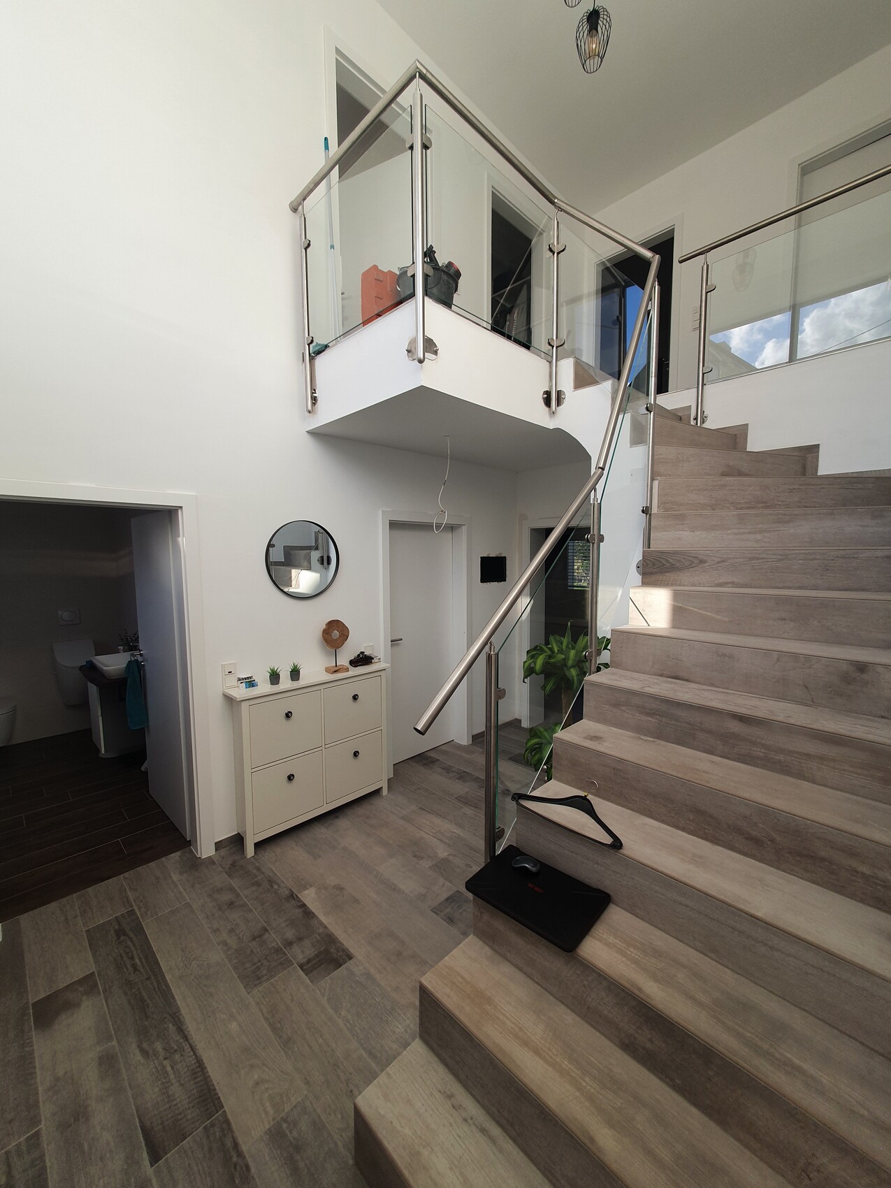 Moderne Eingangshalle mit Holztreppe und Glasgeländer, Sideboard, Spiegel und Pflanzen.
