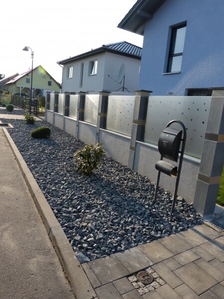Moderne Häuserzeile mit Metallzaun, Kiesgarten und Briefkasten am Gehweg.