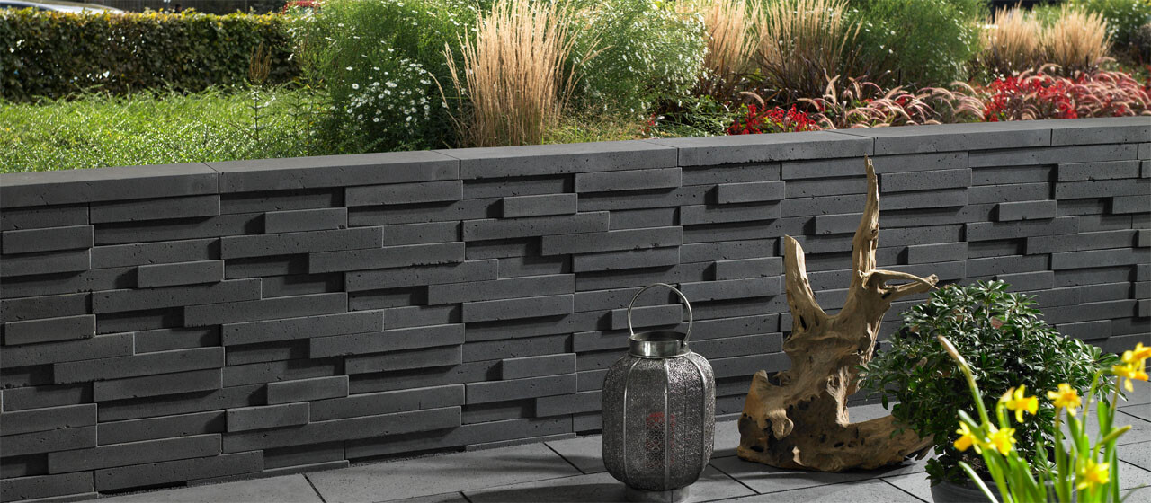Gartenwand aus grauen Blöcken, Laterne, Trockenholz-Skulptur und Topfpflanzen