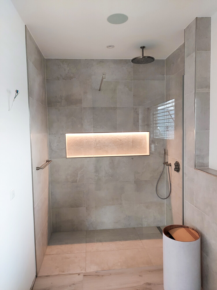 Moderne begehbare Dusche mit grauen Fliesen, Decken-Regenkopf, Handbrause und beleuchteter Nische.