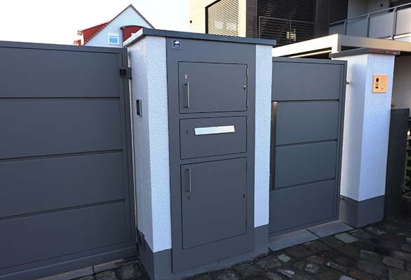 Moderne graue Metall-Gate mit integrierter Briefkasten-/Paketstation zwischen Mauern.