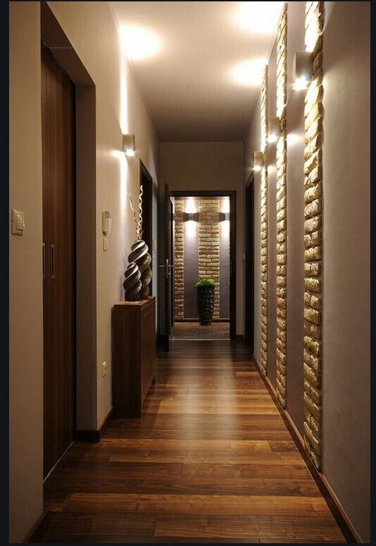 Langer Flur in moderner Wohnung mit Holzboden, Steinwanddetails, Skulptur links und Pflanze am Ende.