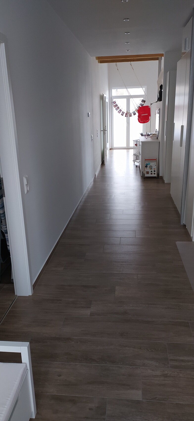 Heller Flur mit Holzboden; am Ende Glas-Tür, Foto-Girlande, roter Rucksack.