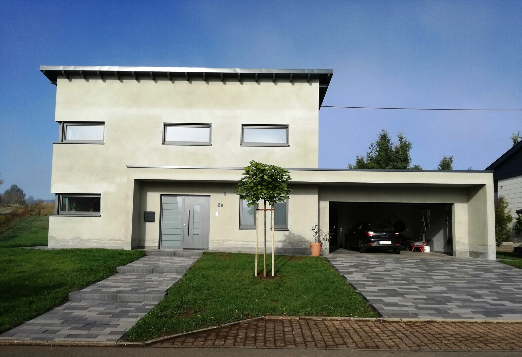 Modernes zweistöckiges Haus mit Garage, gepflasterter Einfahrt und Baum im Vorgarten.