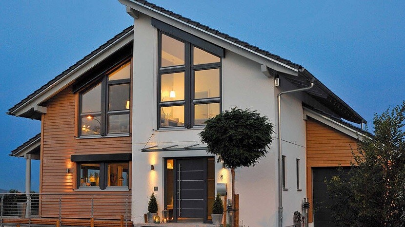 Modernes zweigeschossiges Haus mit großen Fenstern, Holzverkleidung und Abendbeleuchtung.