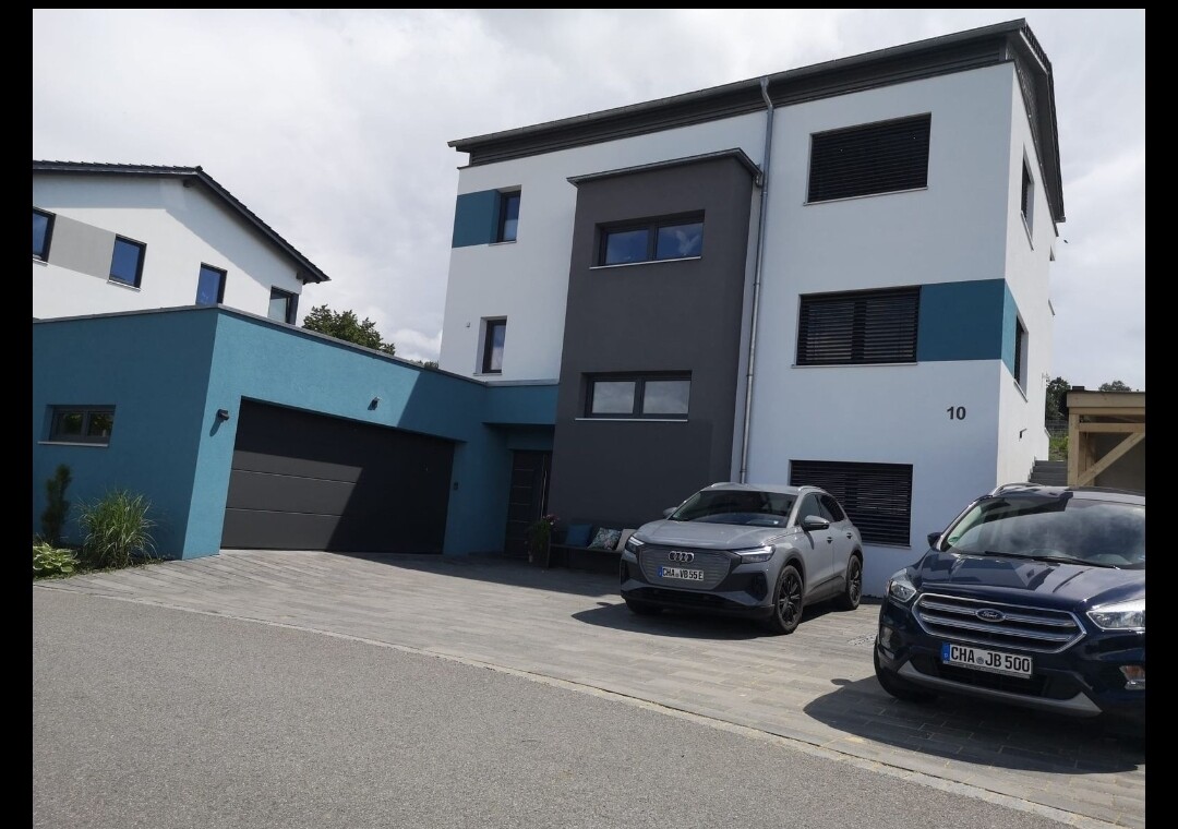 Moderne zweistöckige Hausfront mit Garage und zwei Autos auf der Einfahrt.