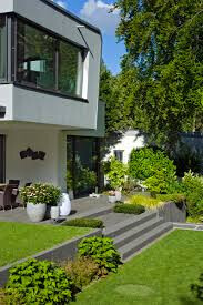 Moderne Haus-Außenansicht mit Terrassenstufen, grünem Garten und Bäumen.