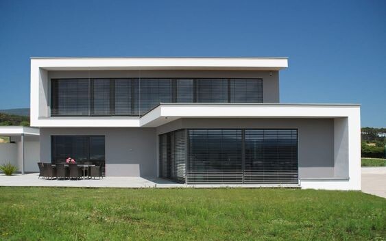 Moderne zweistöckige Hausfassade mit großen Fenstern, Terrasse und grünem Rasen.