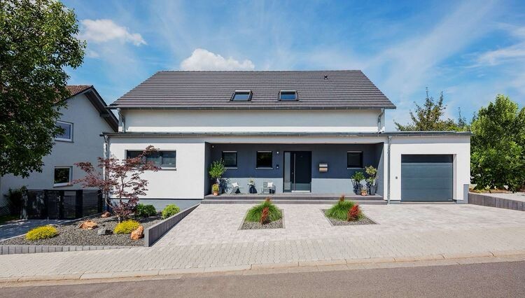 Moderne weiße Doppelhaushälfte mit grauer Fassade, Garage rechts, gepflasterte Einfahrt.