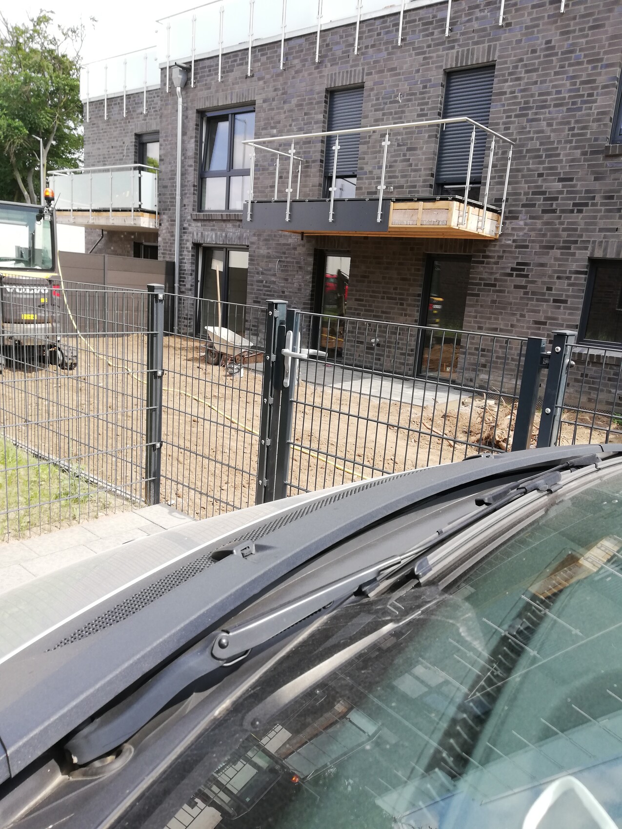 Baustelle vor dunklem Backsteingebäude; Balkon wird montiert; Absperrzaun; Autoscheibe im Vordergrund