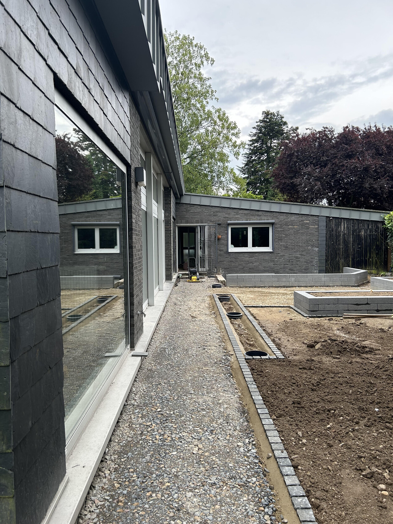 Moderne graue Hausfassade, Kiesweg neben Fensterfront, Gartenbereich im Bau.
