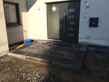 Moderner Hauseingang mit dunkler Tür, seitlichem Fenster und Stein-Treppenstufen