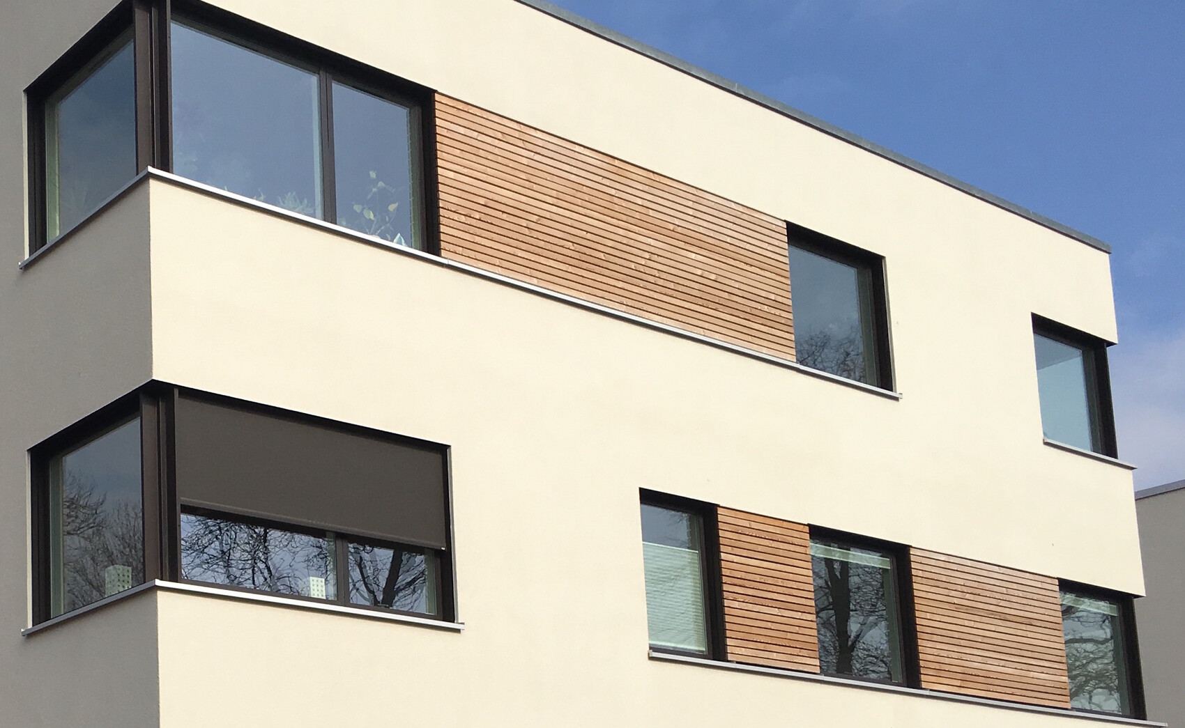 Moderne weiße Hausfassade mit großen Fenstern und Holzlamellen