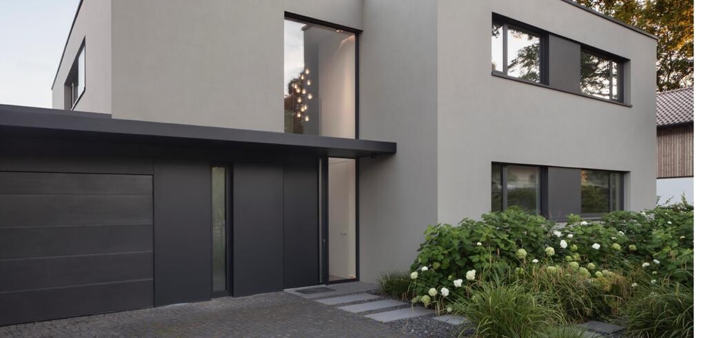 Modernes zweistöckiges Haus mit grauer Fassade, dunkler Garage, Haustür und weißen Hortensien.